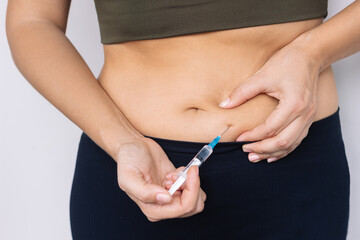 Young woman putting a hormonal injection in her stomach with the syringe on gray background. The...