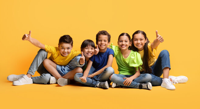 Happy multiethnic kids sitting on floor, showing thumb ups