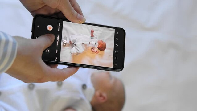 Young mother takes a picture of her newborn baby on mobile phone. baby's photo on cellphone screen.