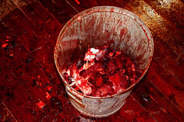 Metal bucket with bloody offal and a lot of blood on the wooden floor