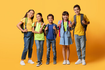 happy boys and girls posing with backpacks posing on yellow