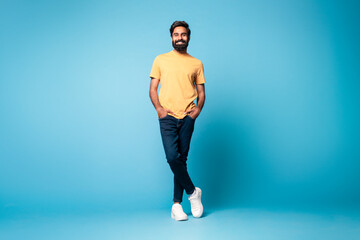 Fototapeta na wymiar Positive handsome middle aged indian man in casual outfit posing with hands in pockets on blue background, full length