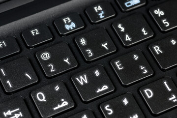 Close up of a QWERTY keyboard english and arabic with letters, figures and symbols, focus on symbol @