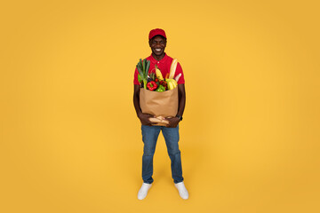 Smiling millennial african american guy courier in uniform hold paper bag with food
