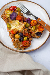 Eggplant baked with meat, tomatoes, olives and mozzarella, sprinkled with basil leaves on a plate with cutlery, on a light background, view from above..