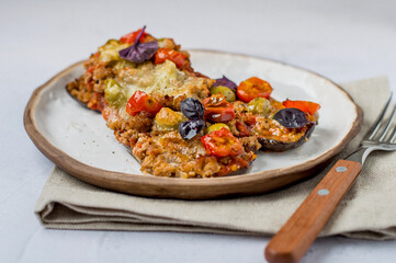 Eggplant baked with meat, tomatoes, olives and mozzarella, sprinkled with basil leaves on a plate with cutlery, on a light background. Serving eggplant on a plate....