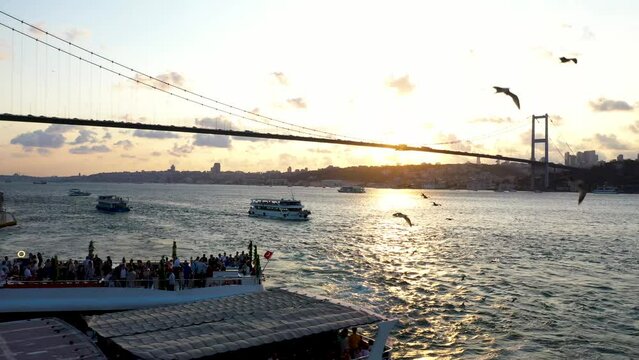 4K footage of Istanbul Strait and suspending Bosphorus bridge during sunset. Shooting from departing boat from pier on the wavy sea with other boats and seagulls stock video.