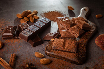 Pieces of chocolate and nuts on a plank on a dark background