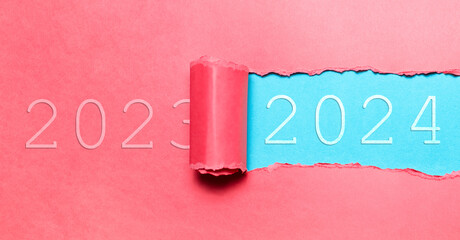 Happy new year, new start; resolution concept. Text of 2024 on cyan background in hole of torn pink paper with text of 2023. Panoramic banner view. Colourful, seasonal concept.