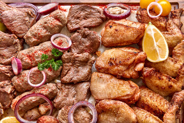 Part of the wooden board with fried meat and vegetables on the wooden table, close-up, shallow depth of field. Beef and chicken meat in focus