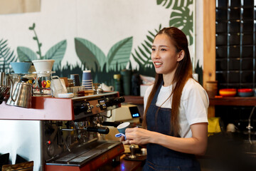 Asian beautiful woman Cleaning and wiping the coffee machine clean before closing the shop in order to be hygienic in order to welcome customers the next day in the cafe. Run a small family business..