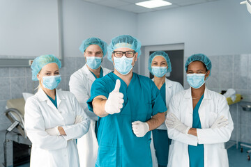 Group of medical professionals standing and looking at camera in the hospital operating room as...
