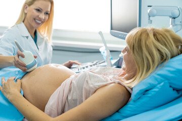Smiling female doctor doing final ultrasound checking to cheerful joyous blonde pregnant woman.