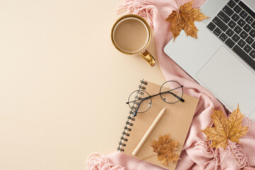Cozy desk arrangement in autumn hues. Top view photo of cute blanket, pen, notebook, laptop, coffee mug, eyewear, autumn leaves on pastel beige background with empty space for promo or text