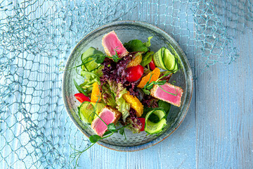 Salad with fresh tuna on a blue background. Mediterranean Kitchen. Sea mood menu.
