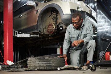 Serious mechanic in grey overall checking car tire