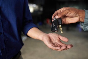 Hands of mechanic giving key to car owner after finishing repairing it