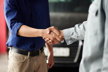 Cropped image of car owner and mechanic shaking hands, greeting each other