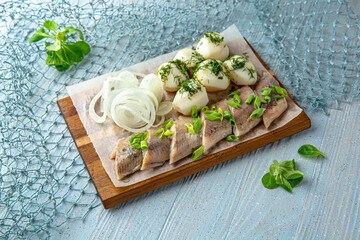 Herring with onions and boiled potatoes on a blue background. Mediterranean Kitchen. Sea mood menu.