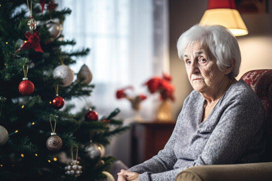 Solitude, Loneliness During Christmas Holidays. Sad Eldery Woman Sitting On Sofa Near Decorated Christmas Tree At Home. Lonely Unhappy Senior Woman Celebrating Christmas Alone, Wihout Family, Friends