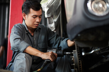 Car service worker in uniform removing lug nuts with impact wrench