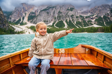 Little girl sitting in big brown boat at Lago di Braies lake in cloudy day, Italy. Summer vacation in Europe