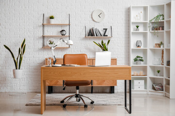 Workplace with laptop, stylish holder for books and lamp in room