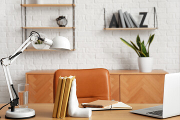 Workplace with laptop, stylish holder for books and lamp in room