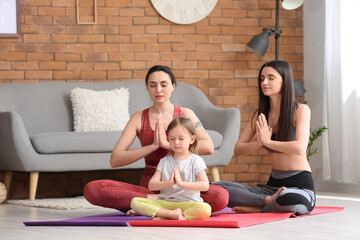 Young lesbian couple with adopted little girl meditating at home