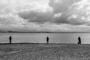 Black and white tone, Outdoor panoramic and silhouette scenery on the beach with three men are fishing against background of overcast sky and north sea on Kronborg beach in Helsingor, Denmark  