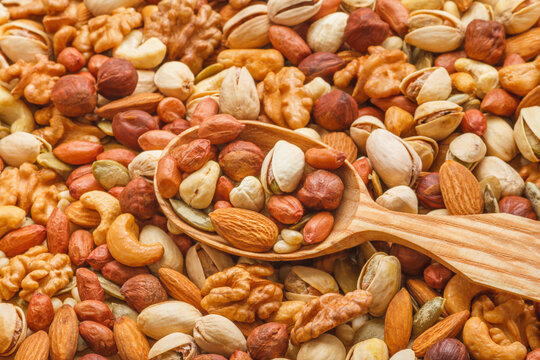Nuts and seeds of different types with a wooden spoon closeup with selective focus - peeled walnut, hazelnuts, peeled peanut, pine nut kernels, almond seeds, cashew seeds