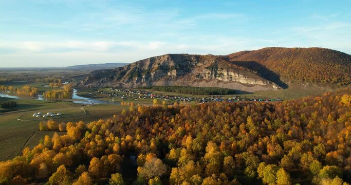 A small village in a picturesque location located near a cliff and a river. Autumn forest on the background of mountains. Aerial shot. The nature of the southern Urals in the autumn season. Drone view