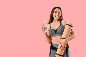 Sporty young woman with bottle of water and fitness mat on pink background