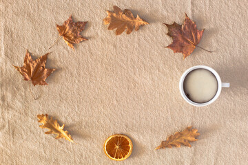 Autumn or winter composition with a cup of coffee, autumn dry leaves, dried orange laid out in a circle on a linen fabric background. Flat lay, copy space, Autumn, fall concept.