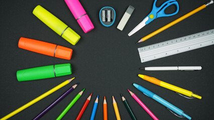 Various colorful school supplies lie in a circle on a black background. Back to school concept