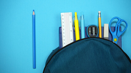 School bag with school supplies on blue background. Back to school concept