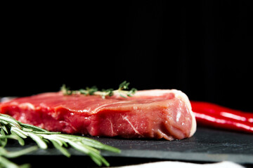 Raw organic beef meat with rosemary, seasonings, salt and red pepper  on black background