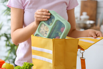 Woman packing fresh meal into lunch box bag in kitchen