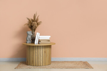 Books, vase with pampas grass and decor on table near beige wall