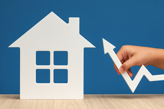 Raising mortgage interest rates. Increasing the bank's margin when buying real estate. A white house symbol with a graph arrow pointing up, on a blue background, close-up. Copy space.