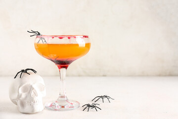 Glass of tasty Margarita cocktail for Halloween with skull and spiders on light background