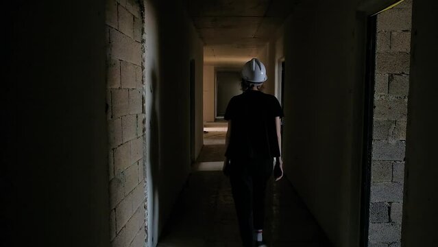 Dark hallway of brick building under construction, female worker going through
