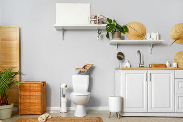Interior of light restroom with ceramic toilet bowl, sink and vanity cabinets