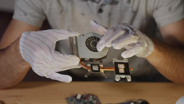 Blogger demonstrates to subscribers laptop cooling system with heat pipes, dusty cooler and thermal paste residue. Techno blog about computer maintenance and man in antistatic gloves at table.