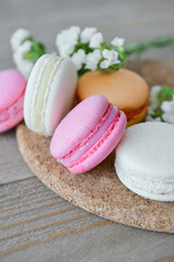 Board with sweet macaroons and beautiful flowers on grey wooden background