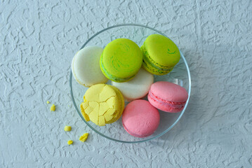 Glass plate with sweet macaroons on light blue background