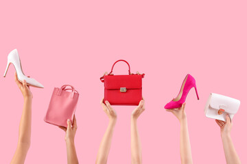 Female hands holding stylish women's bags and shoes on pink background