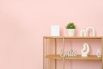 Wooden shelving unit with blank frame and decor near pink wall