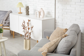 Interior of light living room with grey sofa, standard lamp and white sideboard