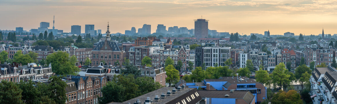 Panorama of Amsterdam, view of traditional canal houses along the Amstel river and modern high-rise buildings in the Zuidas financial district in the background by sunset